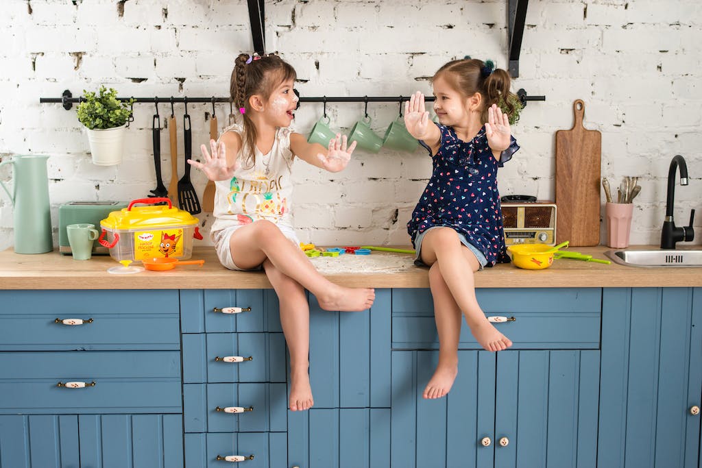 Two Girls Sitting on a Kitchen Counter with Arms Raised