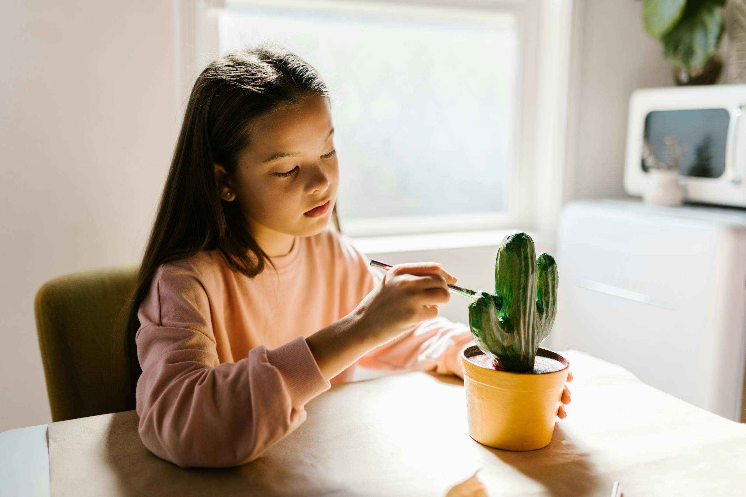 A young girl painting a cactus model indoors, enjoying a creative craft activity in natural light.